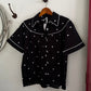 Black blouse with white polka dots on a hanger against a white wall.