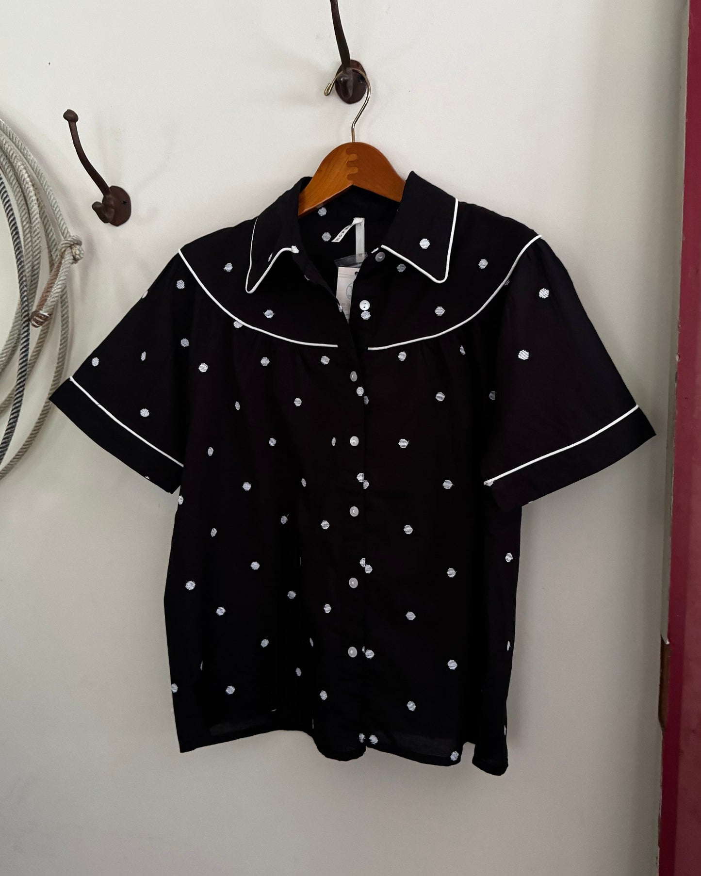 Black blouse with white polka dots on a hanger against a white wall.
