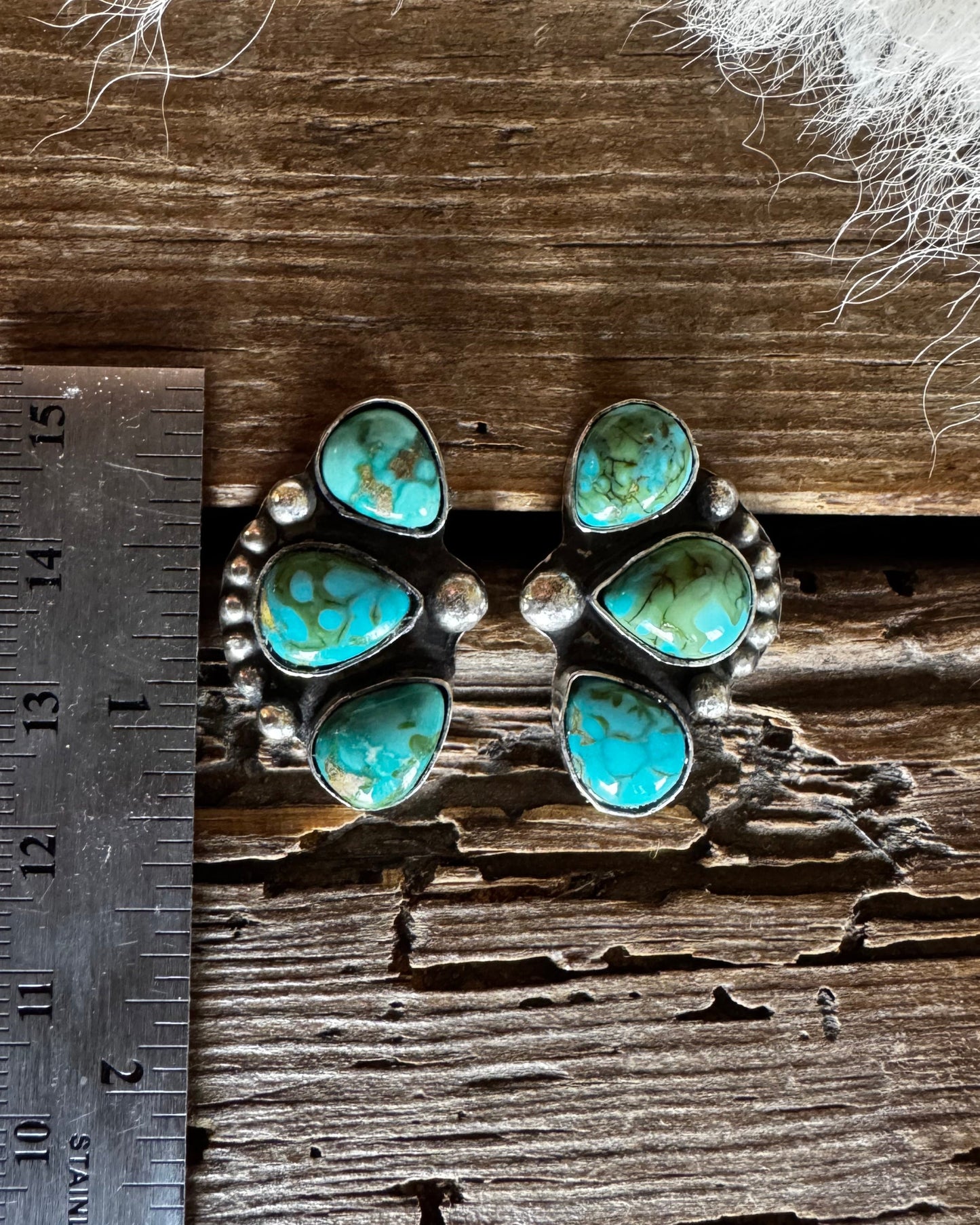 Pair of turquoise earrings on a wooden surface with a ruler for scale.