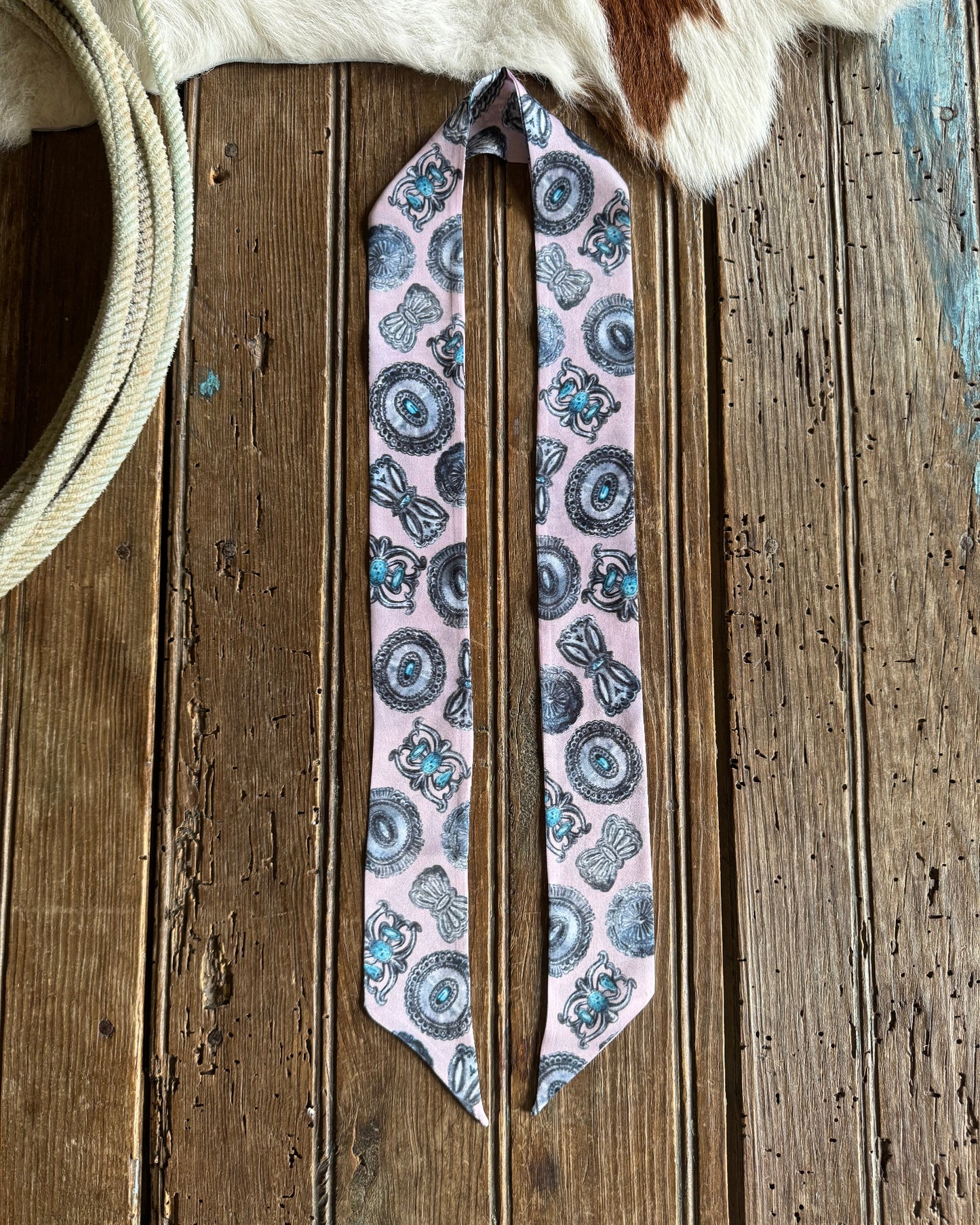 patterned ribbon scarf on a wooden surface with a cowhide rug in the background.
