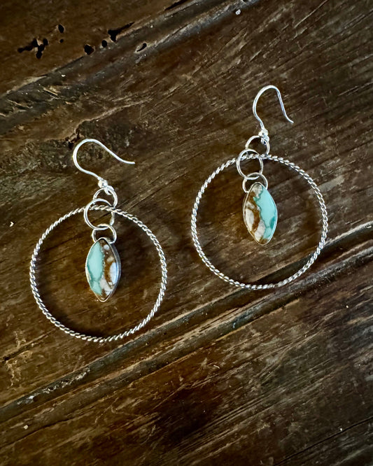 Silver hoop earrings with turquoise stones on a wooden surface