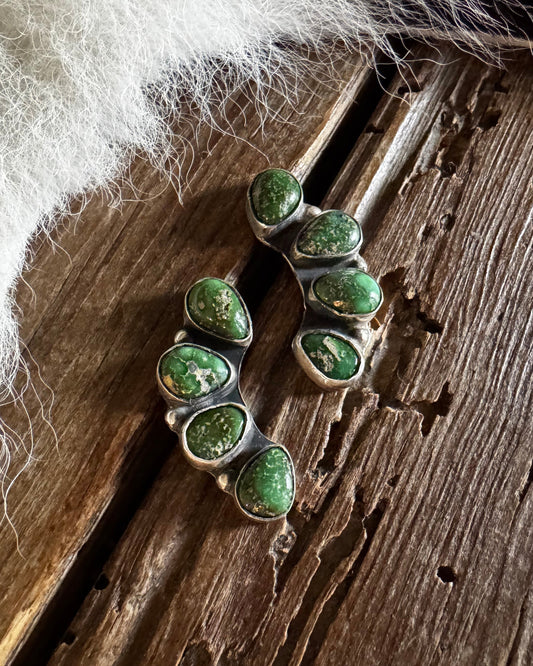 Green gemstone earrings on a wooden surface with fur