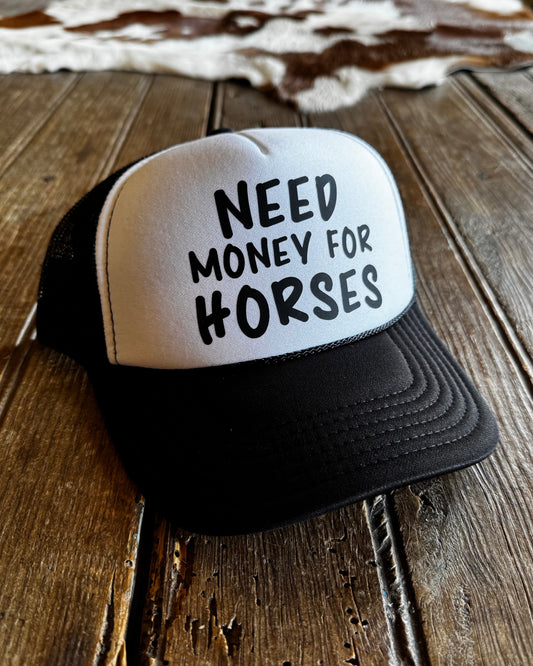 Trucker hat with 'Need Money for Horses' text on a wooden surface
