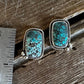 A pair of rectangular turquoise stud earrings with silver bezel settings, displayed on a rustic wooden surface next to a metal ruler for scale.