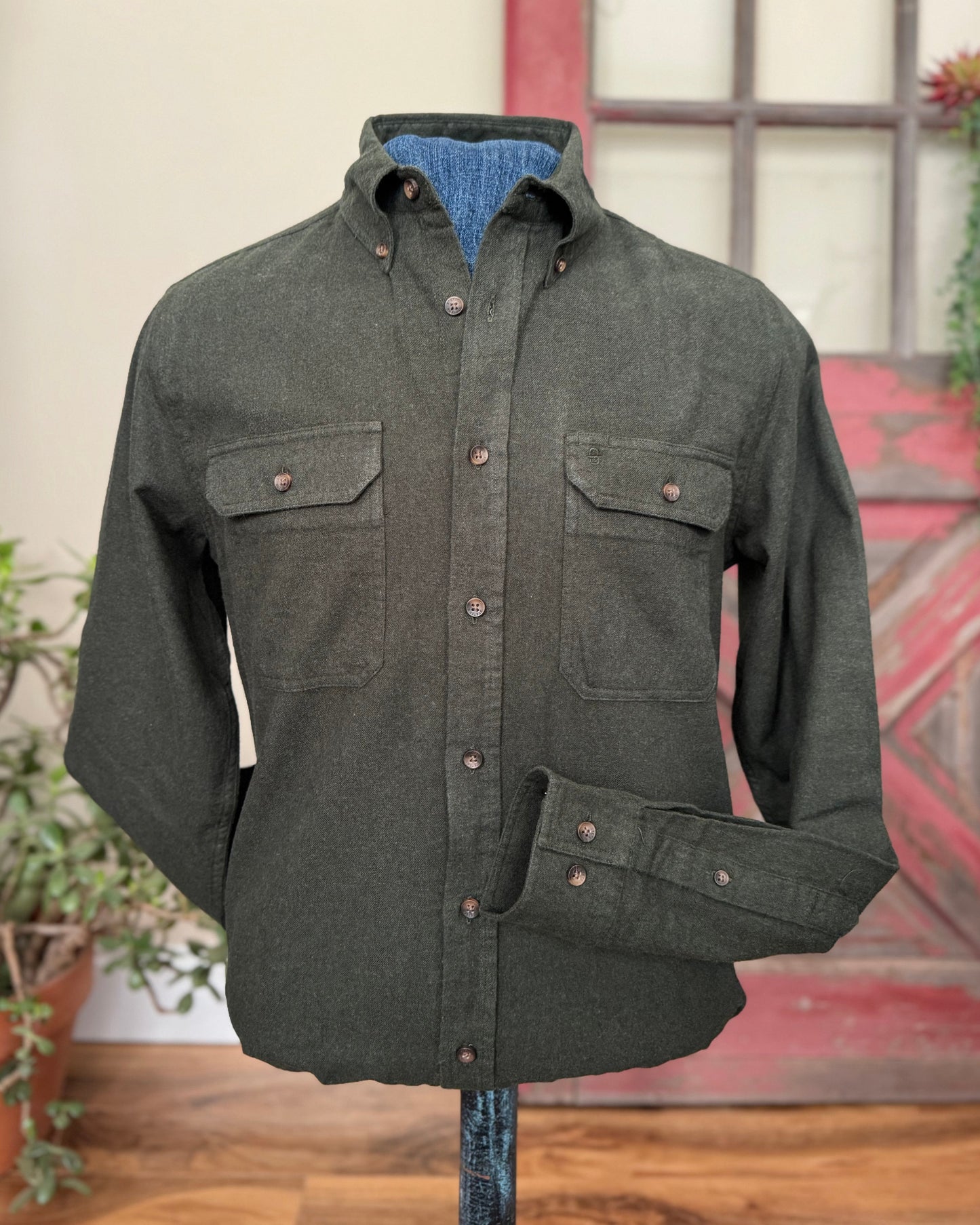 Dark green shirt with button details on a stand against a rustic background