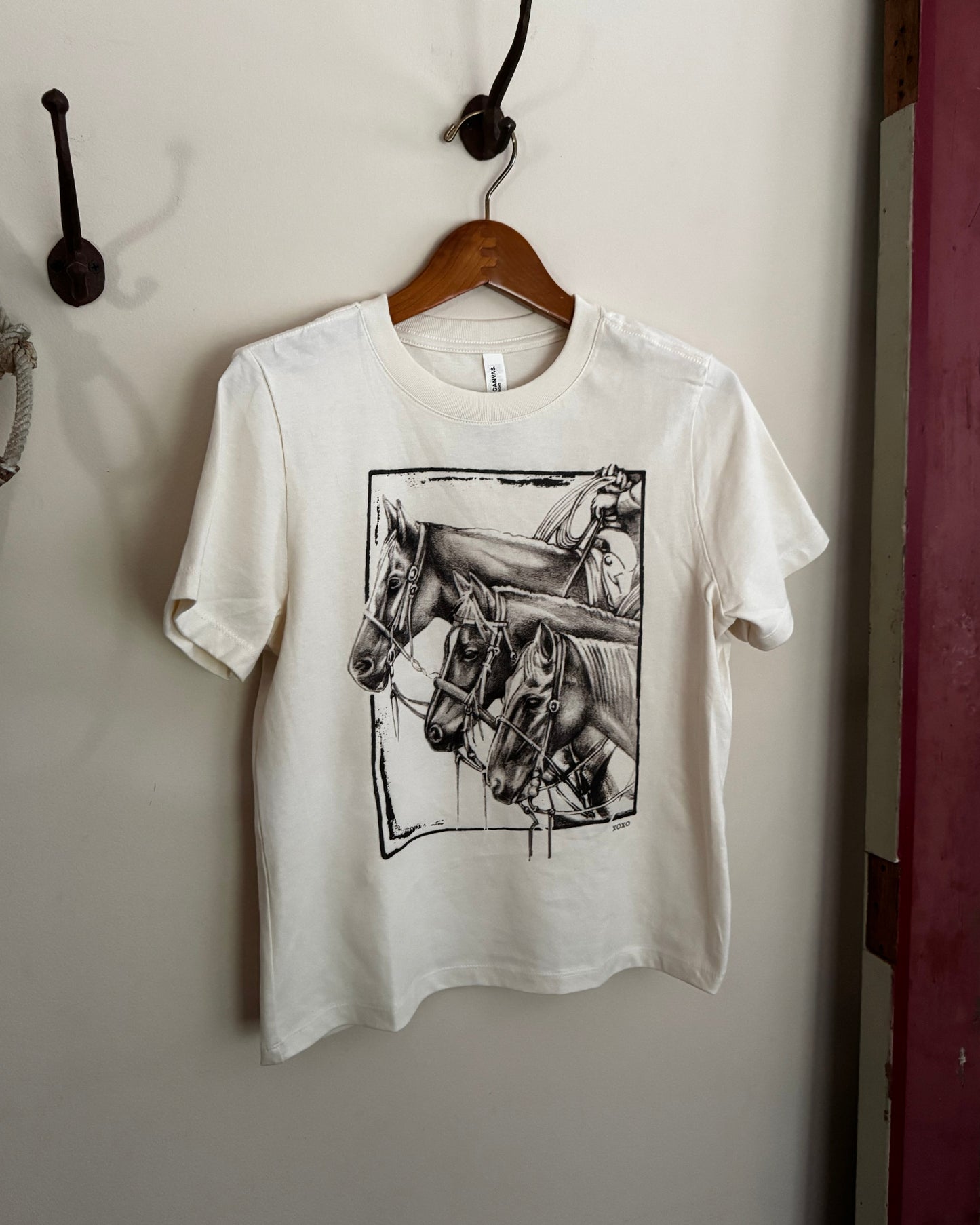 White sweatshirt with black graphic design on a hanger against a white wall.