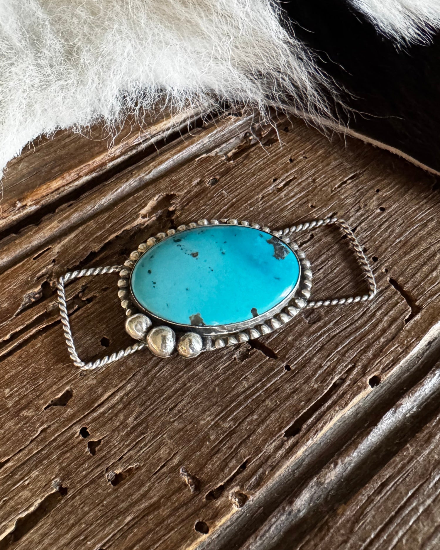 Turquoise stone pendant on a wooden surface with fur in the background