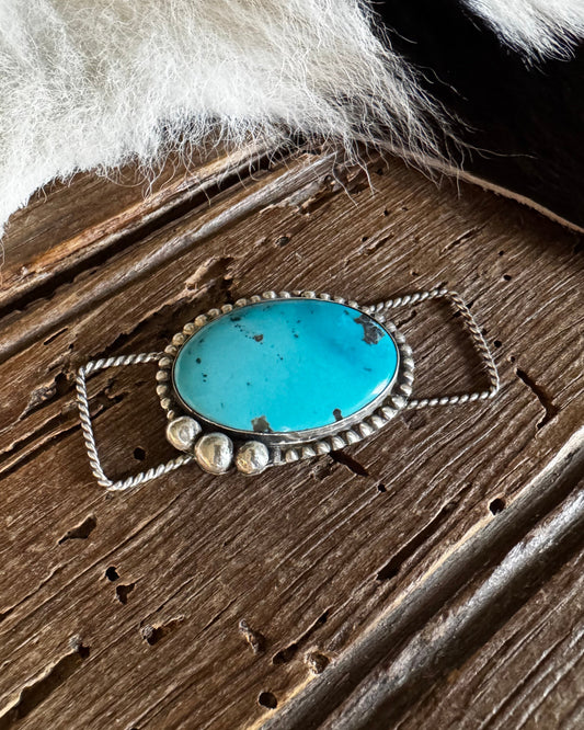 Turquoise stone pendant on a wooden surface with fur in the background