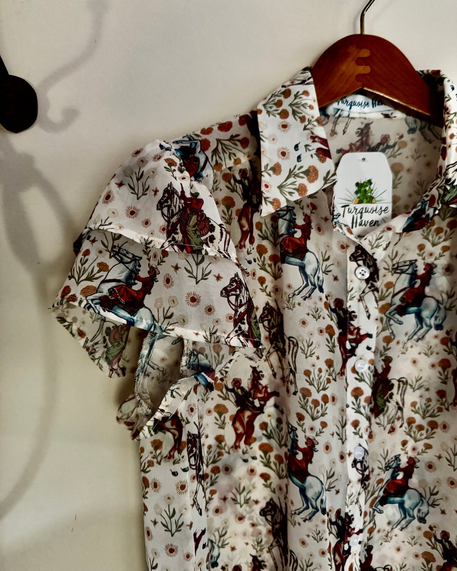 Floral and horse-patterned shirt on a hanger against a white wall