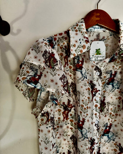 Floral and horse-patterned shirt on a hanger against a white wall