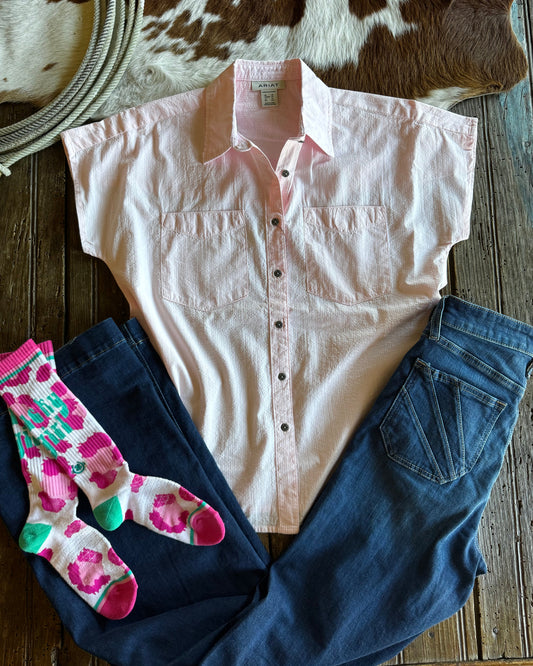 Pink shirt, blue jeans, and colorful socks on a wooden surface with a cowhide rug.