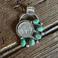 Pendant with green gemstones on a coin, placed on a wooden surface