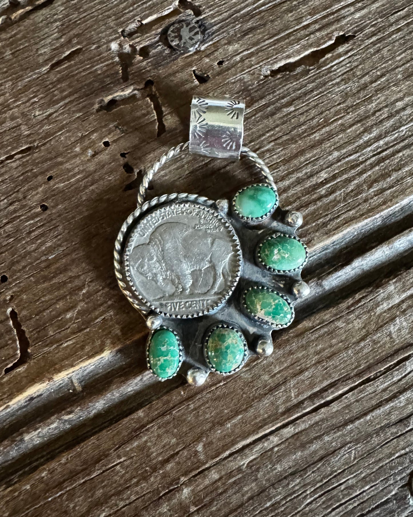 Pendant with green gemstones on a coin, placed on a wooden surface