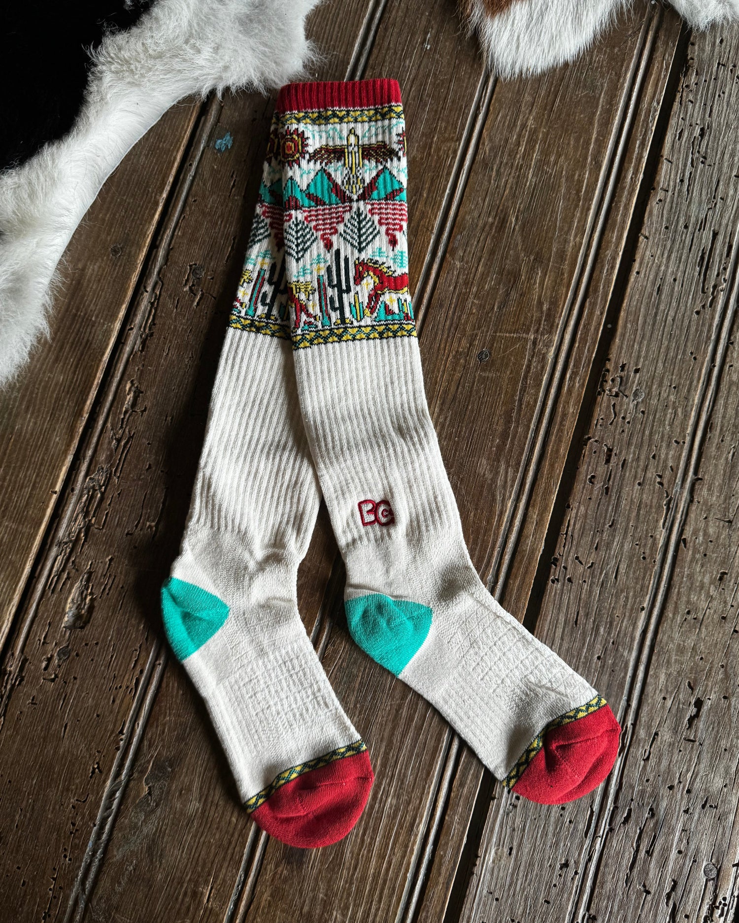 Pair of patterned socks with red, green, and multicolor design on a wooden surface.