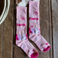 Pink Christmas-themed socks on a wooden surface with a cowhide rug underneath.