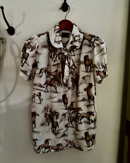 Horse-patterned shirt hanging on a hook against a white wall