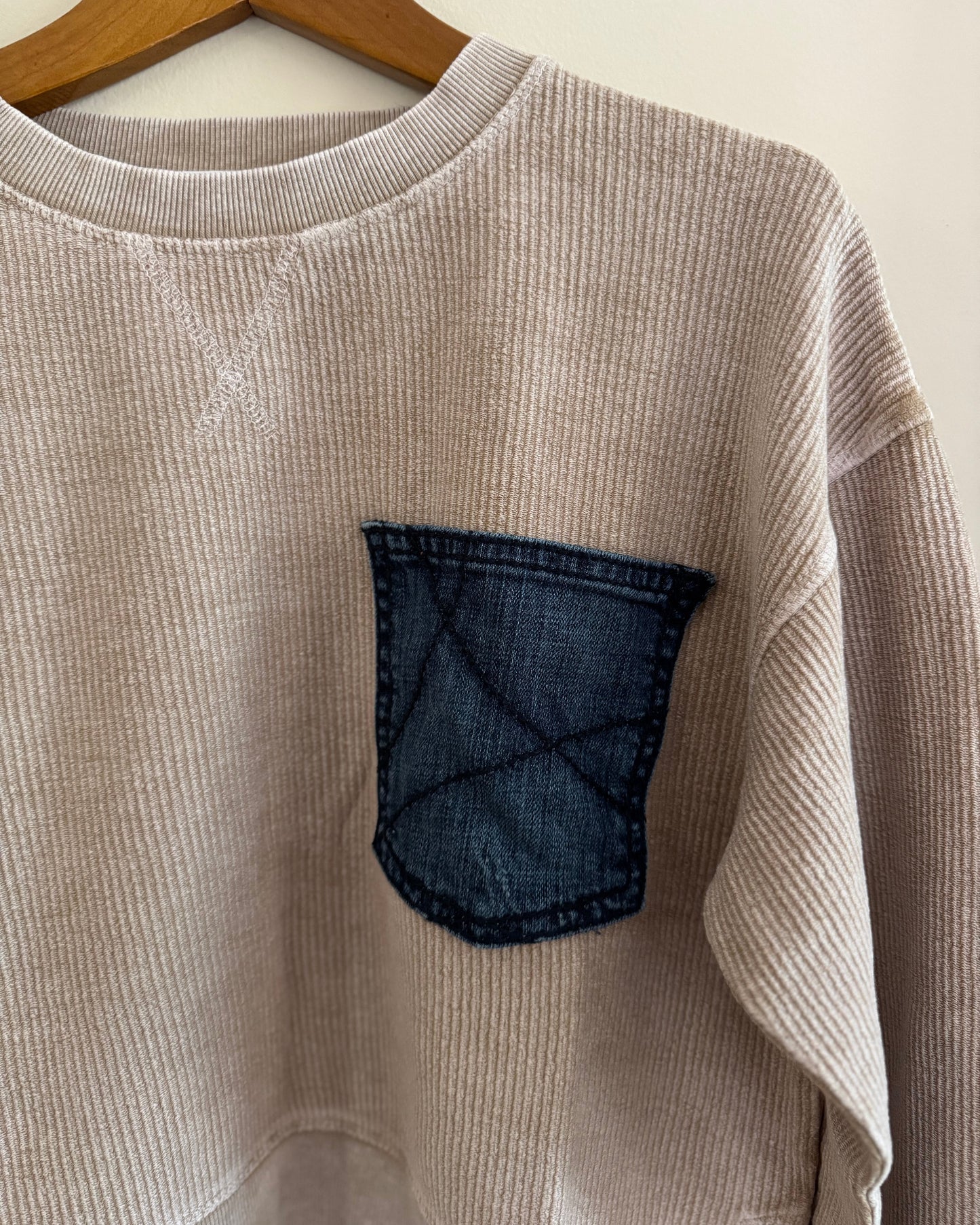 Beige sweater with a denim pocket on a hanger against a white background