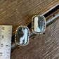 Pair of earrings with stone-like centers on a wooden surface with a ruler for scale.