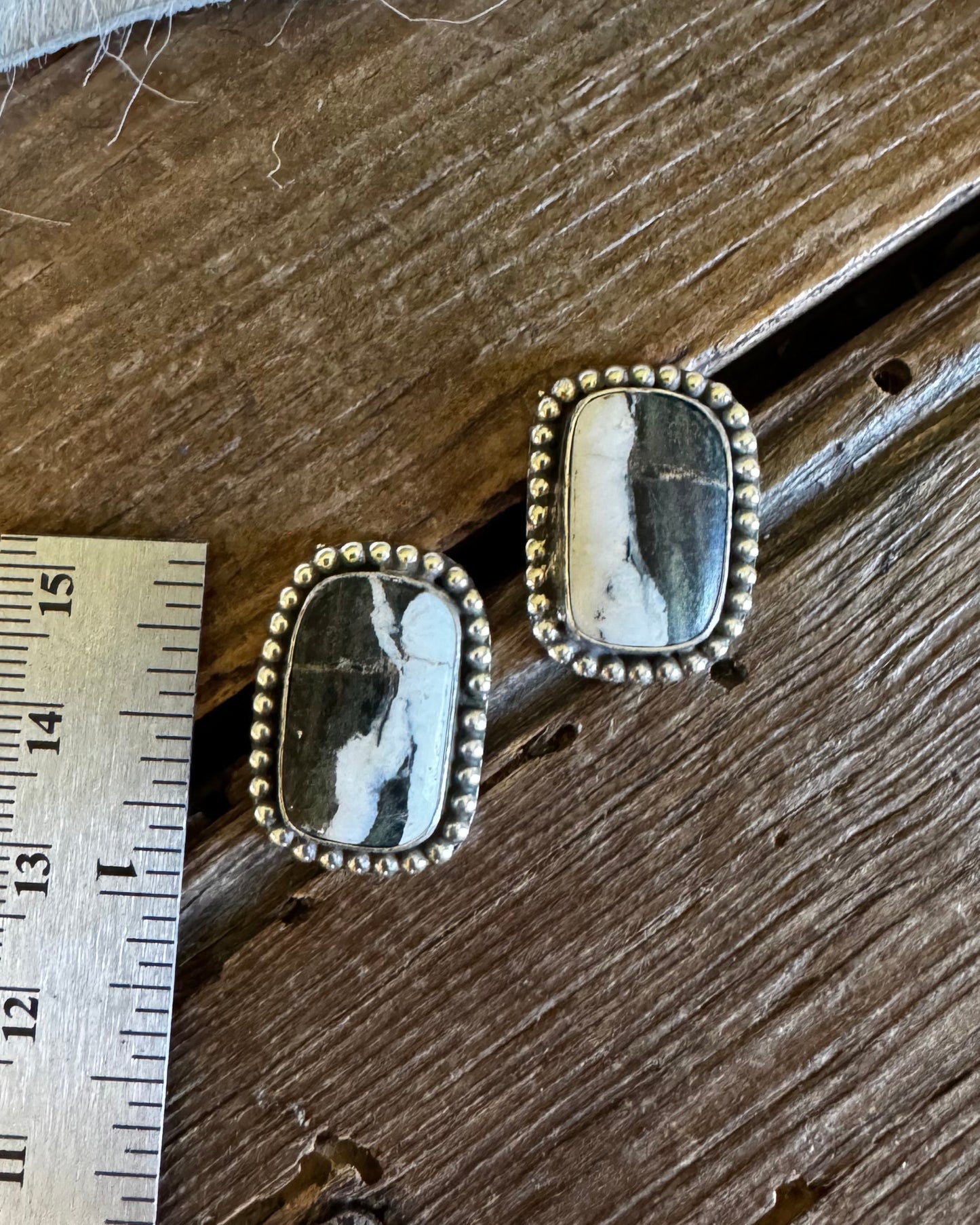Pair of earrings with stone-like centers on a wooden surface with a ruler for scale.