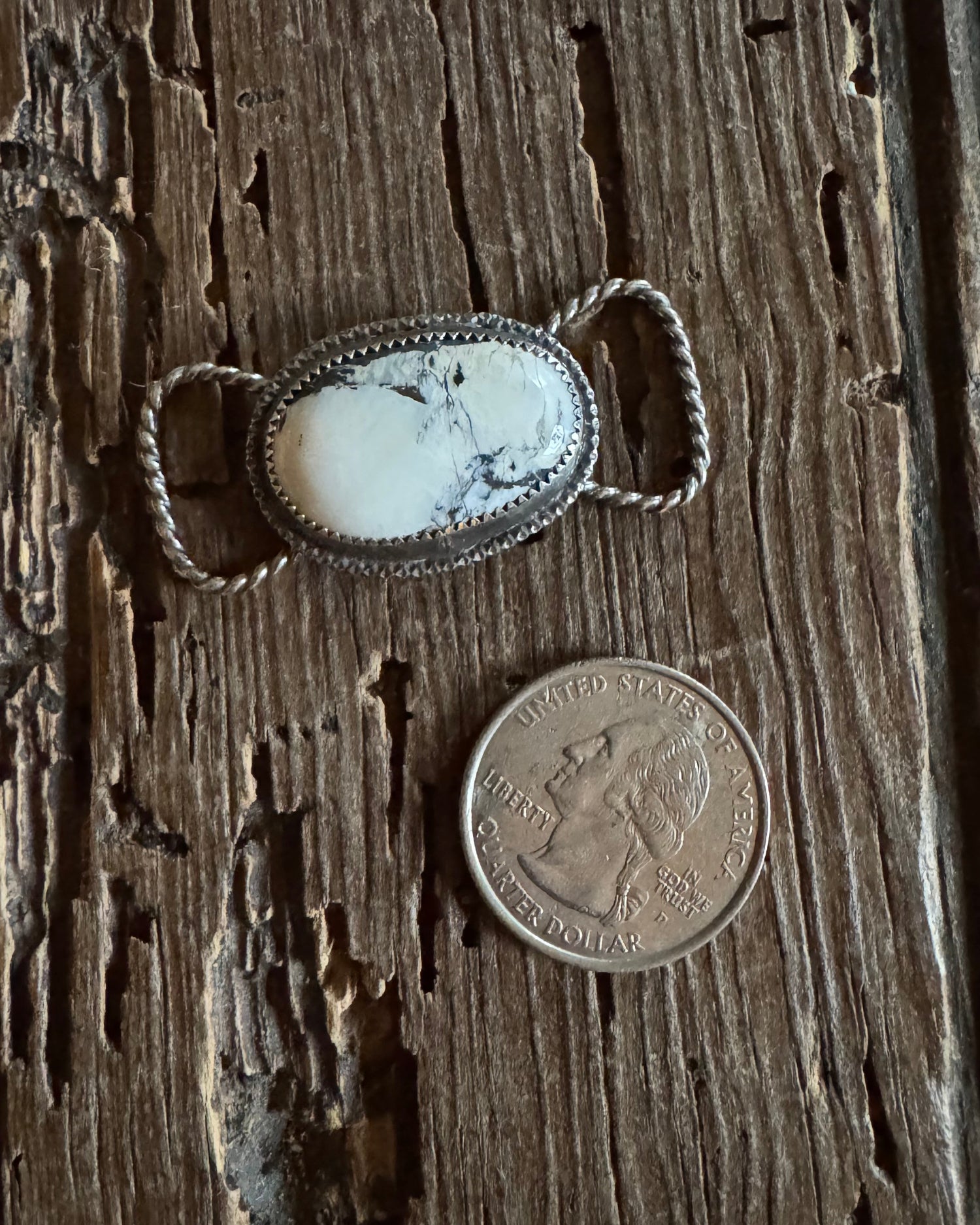 Silver twilly slide and coin on a textured wooden surface