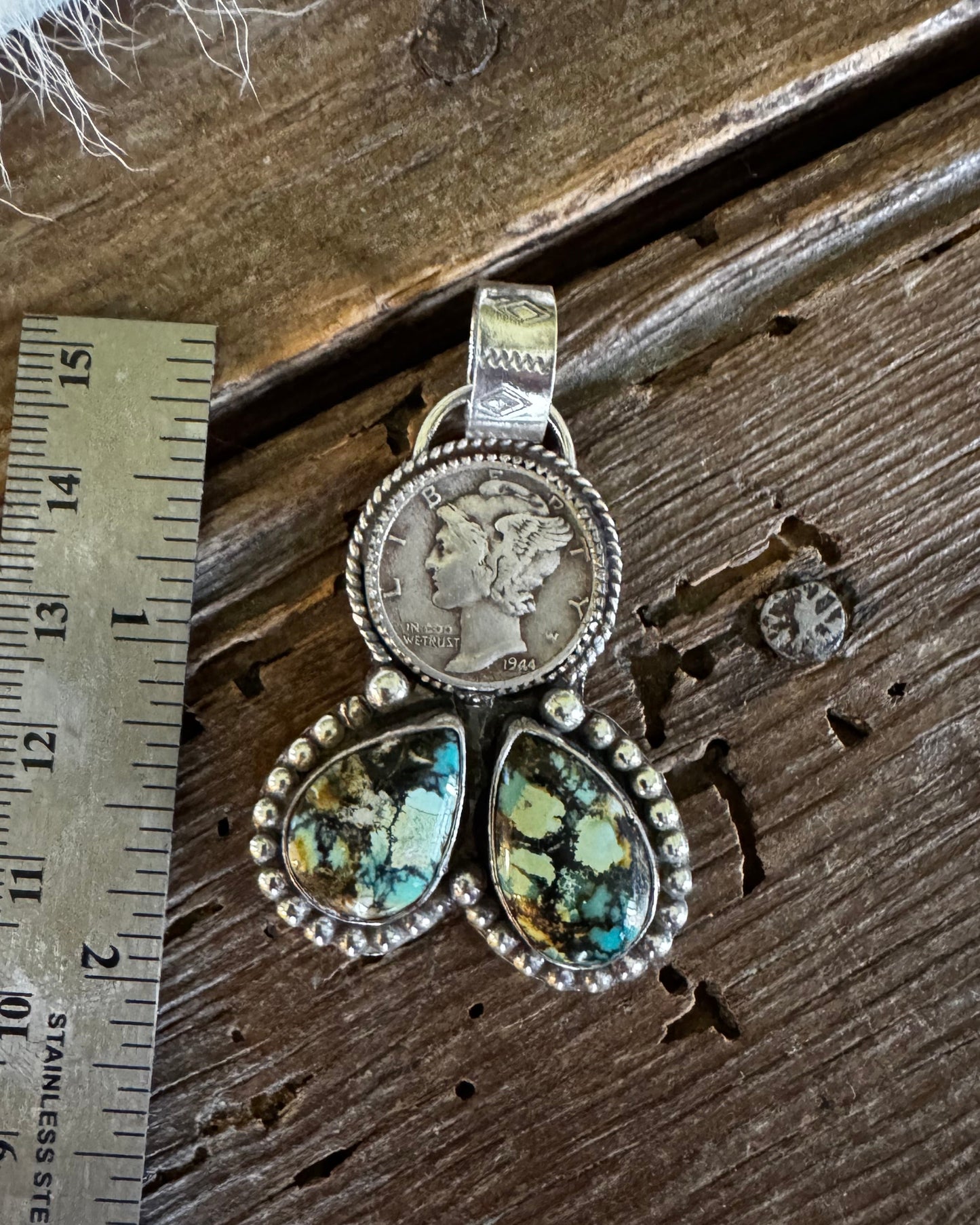 A sterling silver pendant featuring a coin-set oval and three marquise-shaped green iridescent stones, displayed on a rustic wooden surface next to a metal ruler for scale.