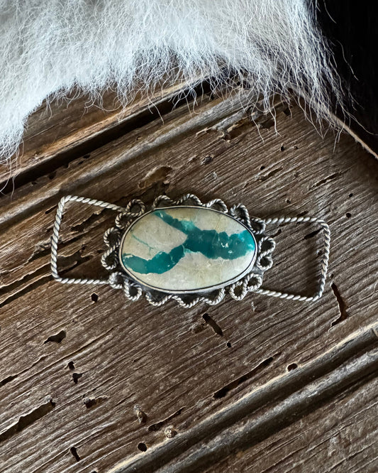Silver pendant with a green stone on a wooden surface