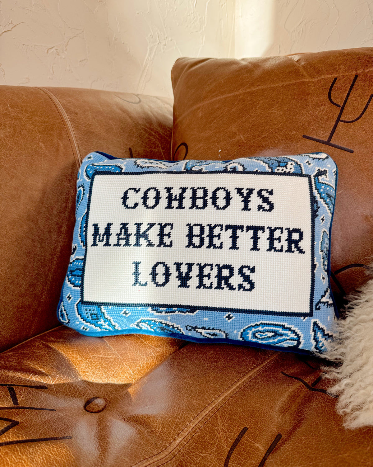 Decorative pillow with 'Cowboys Make Better Lovers' text on a brown couch.