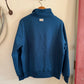 Blue sweatshirt hanging on a hook against a white wall.