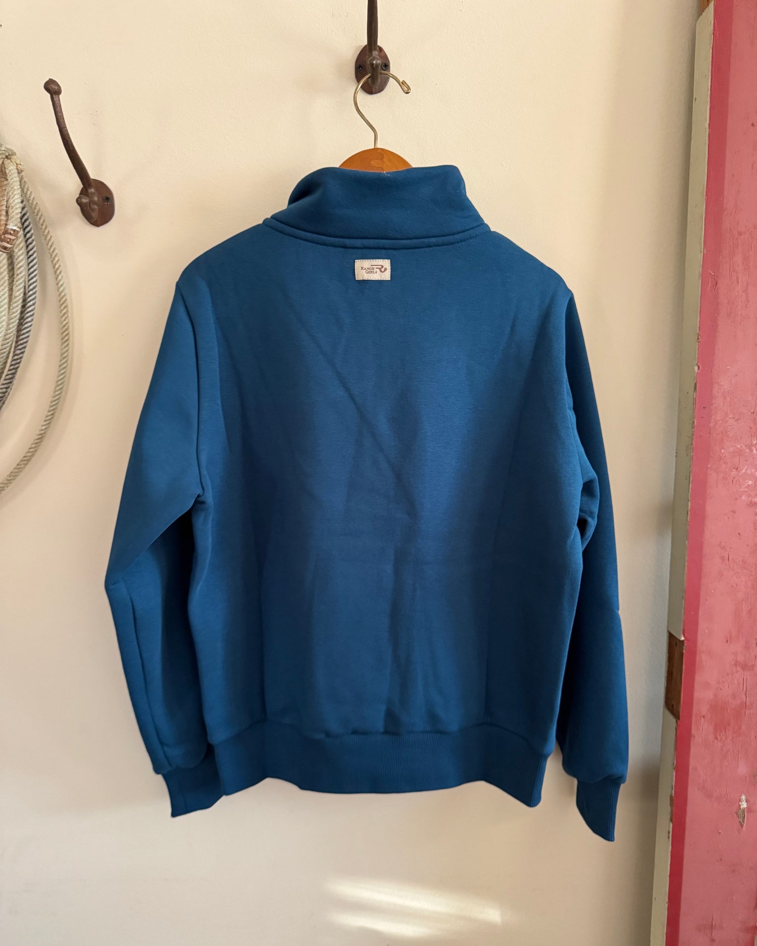 Blue sweatshirt hanging on a hook against a white wall.