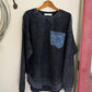 Folded black sweater with a patch on a wooden hanger against a white wall.