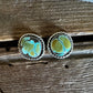 A pair of oval stud earrings with turquoise-blue and yellow marbled stones in a twisted silver-tone metal setting, displayed on a rustic wooden surface.