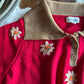 Red garment with beige collar and flower embroidery, featuring the brand 'emergi'.