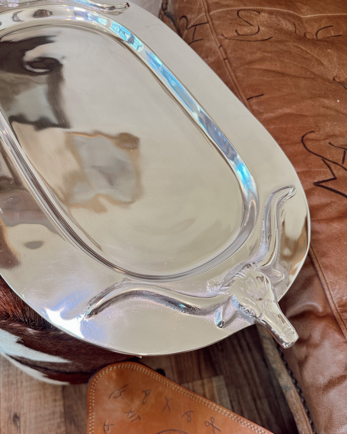 Silver tray on a wooden surface with a leather item underneath
