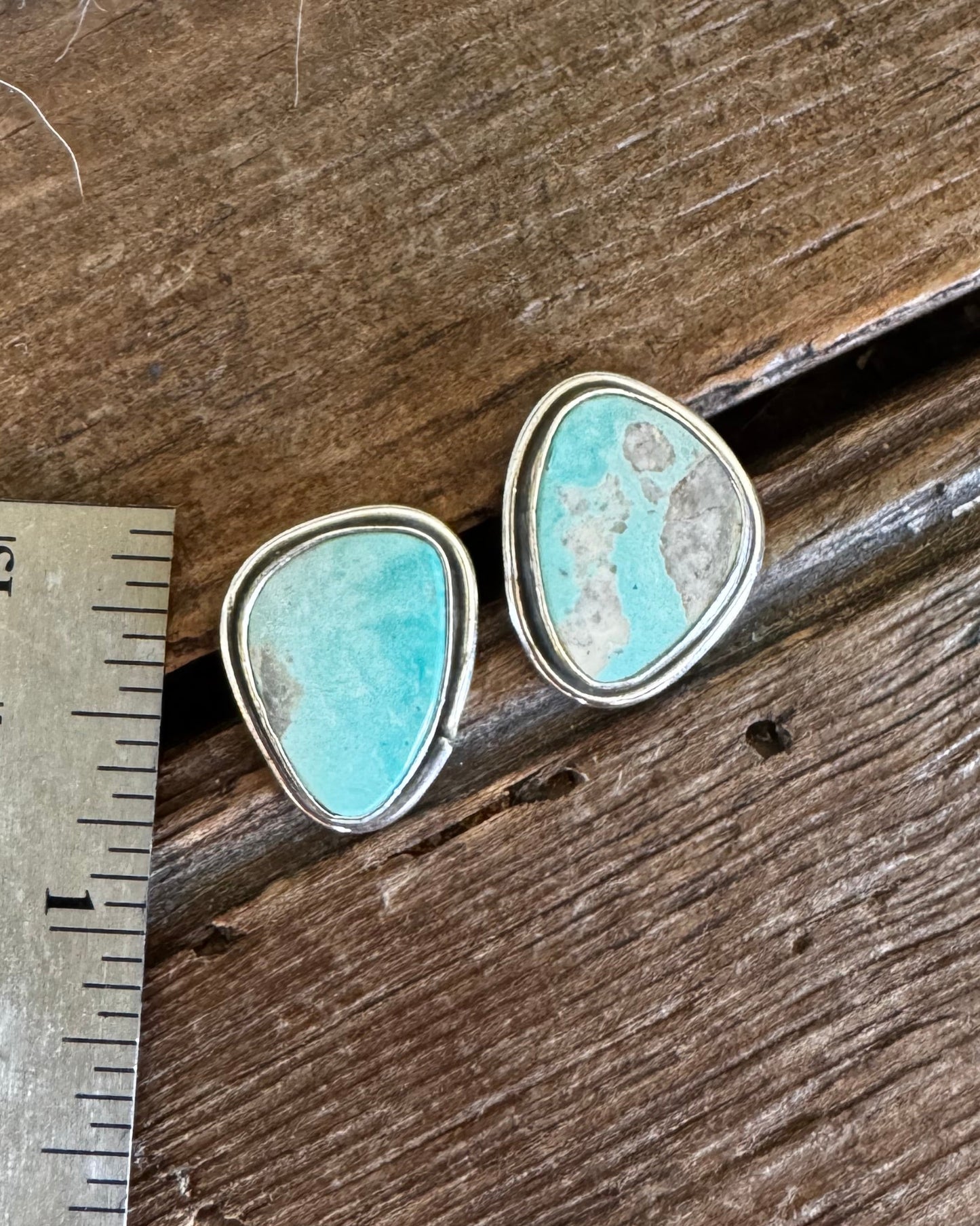 Turquoise stone earrings on a wooden surface with a ruler for scale.
