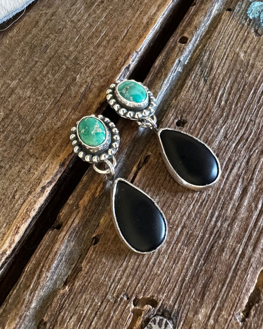 Pair of earrings with green gemstones and black teardrop shapes on a wooden surface.