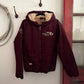 Maroon jacket with fur-lined hood hanging on a hook against a white wall.