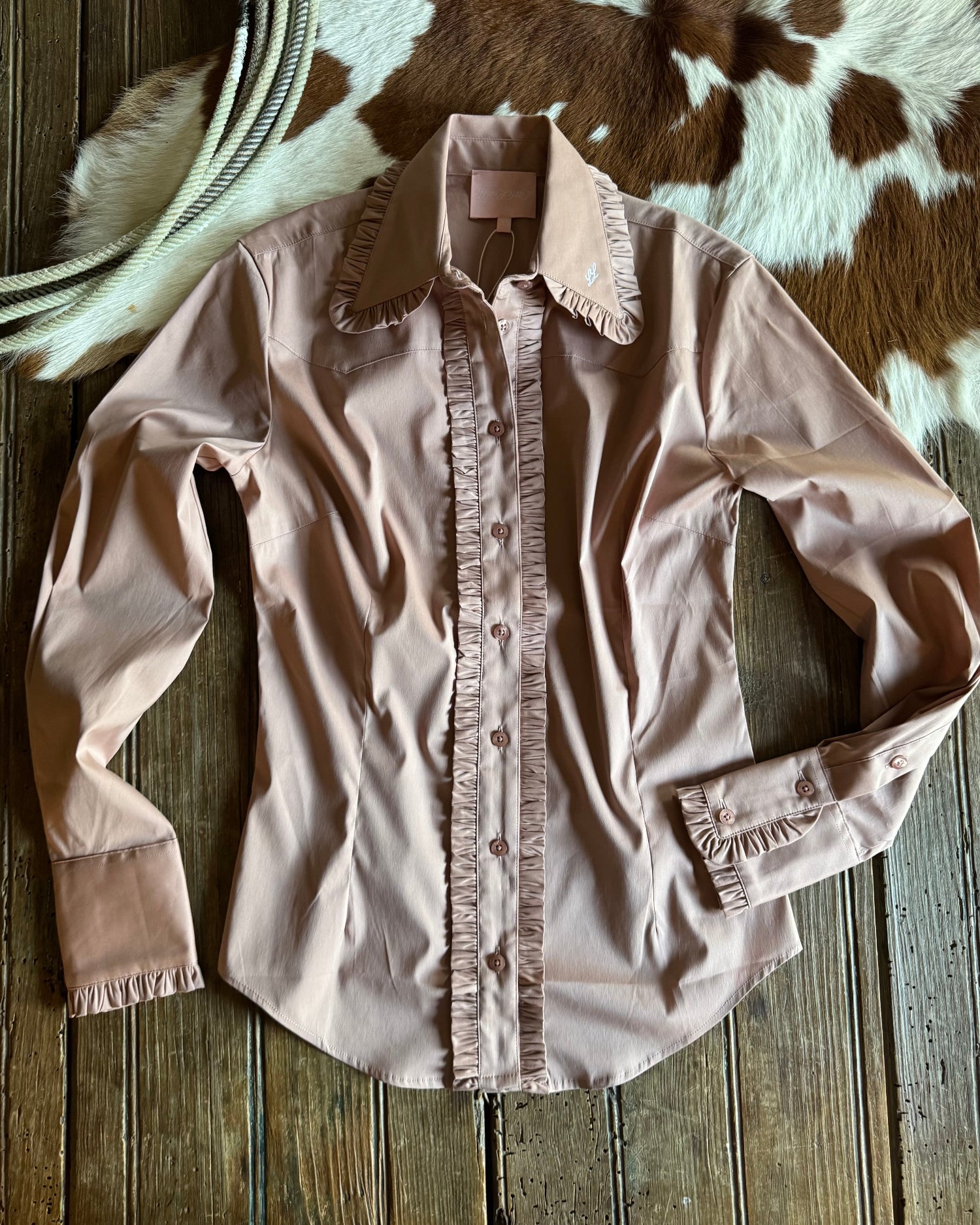 Pink blouse with ruffled details on a wooden surface with cowhide rug in the background