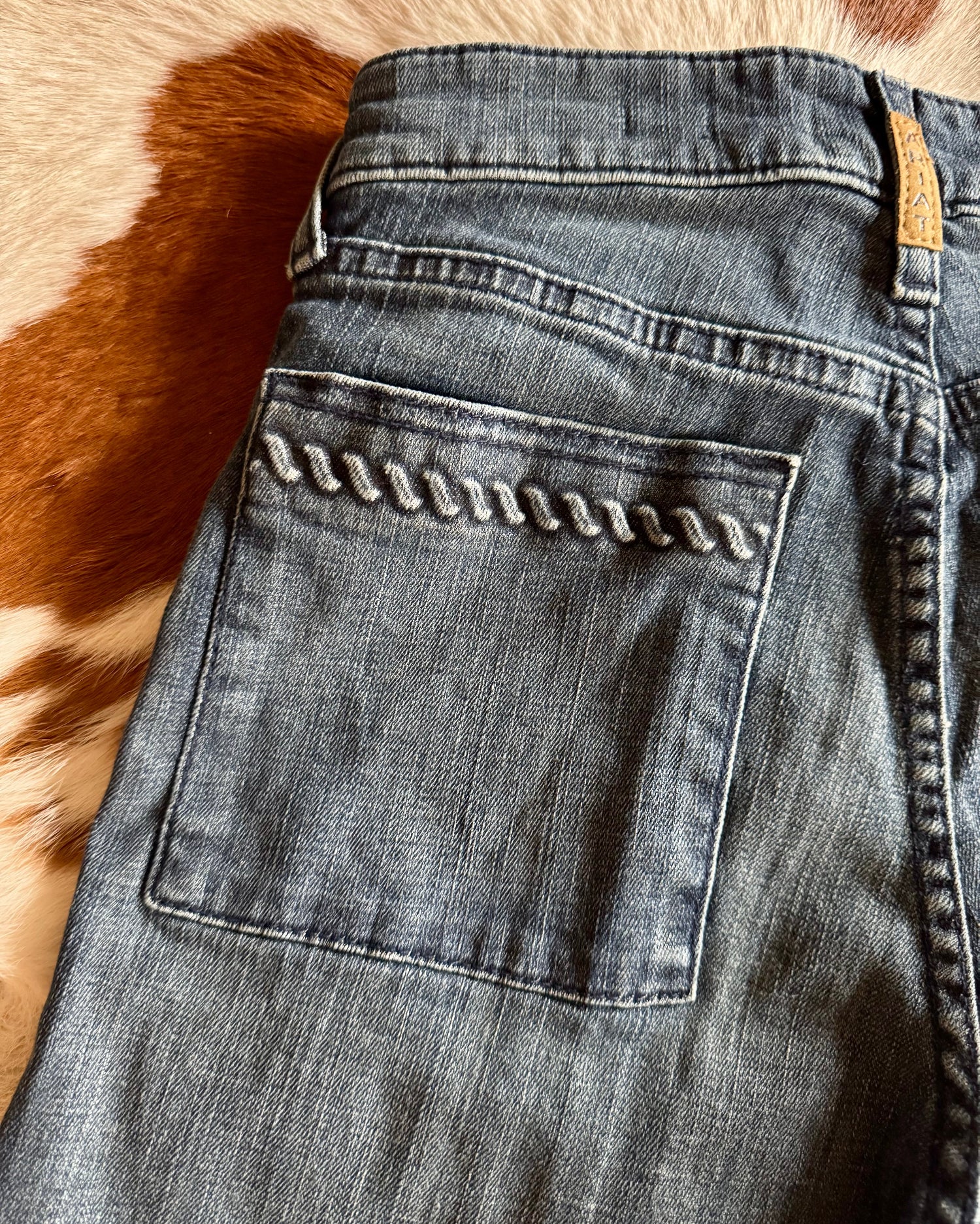 Close-up of a pair of blue jeans with a decorative button on a fur surface