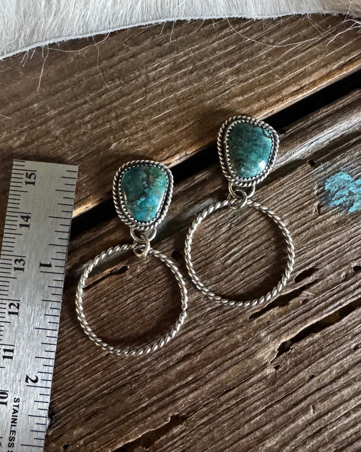Pair of silver earrings with turquoise stones on a wooden surface with a ruler for scale.