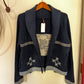 A dark navy blue knit cardigan with a shawl collar, featuring geometric star patterns near the hem and striped detailing on the chest, hanging on a wooden hanger against a cream-colored wall.