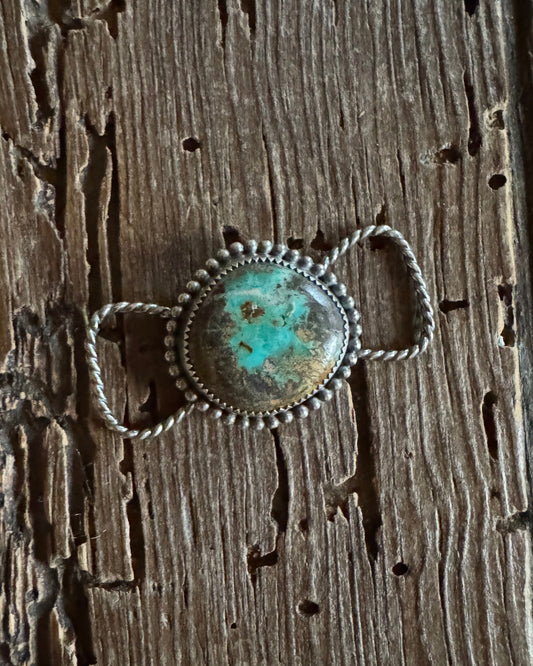 Silver twilly slide with a turquoise stone on a wooden surface