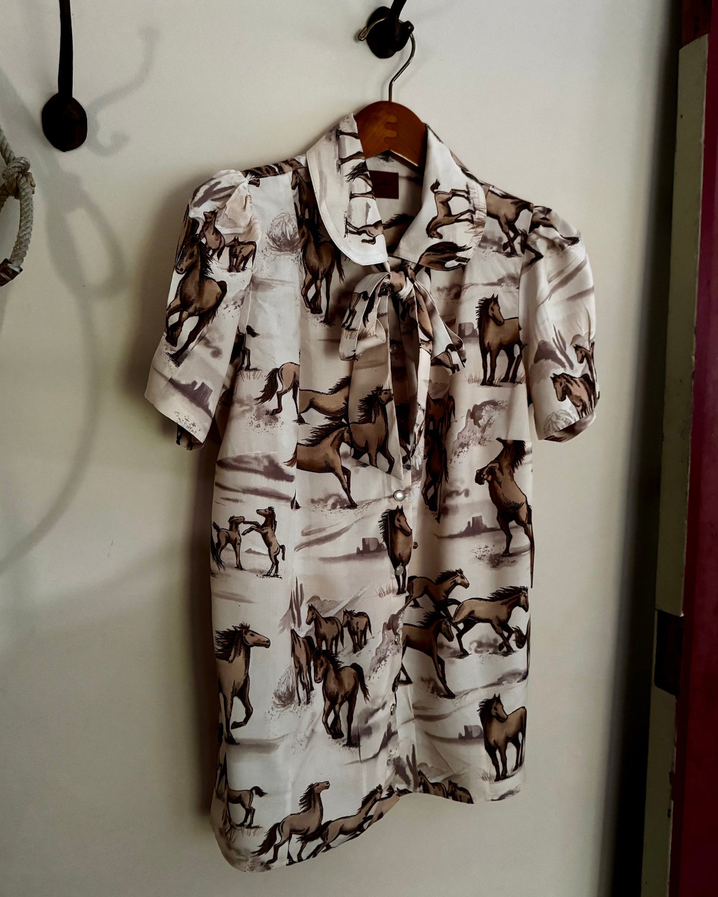 Shirt with horse pattern hanging on a hook against a white wall.