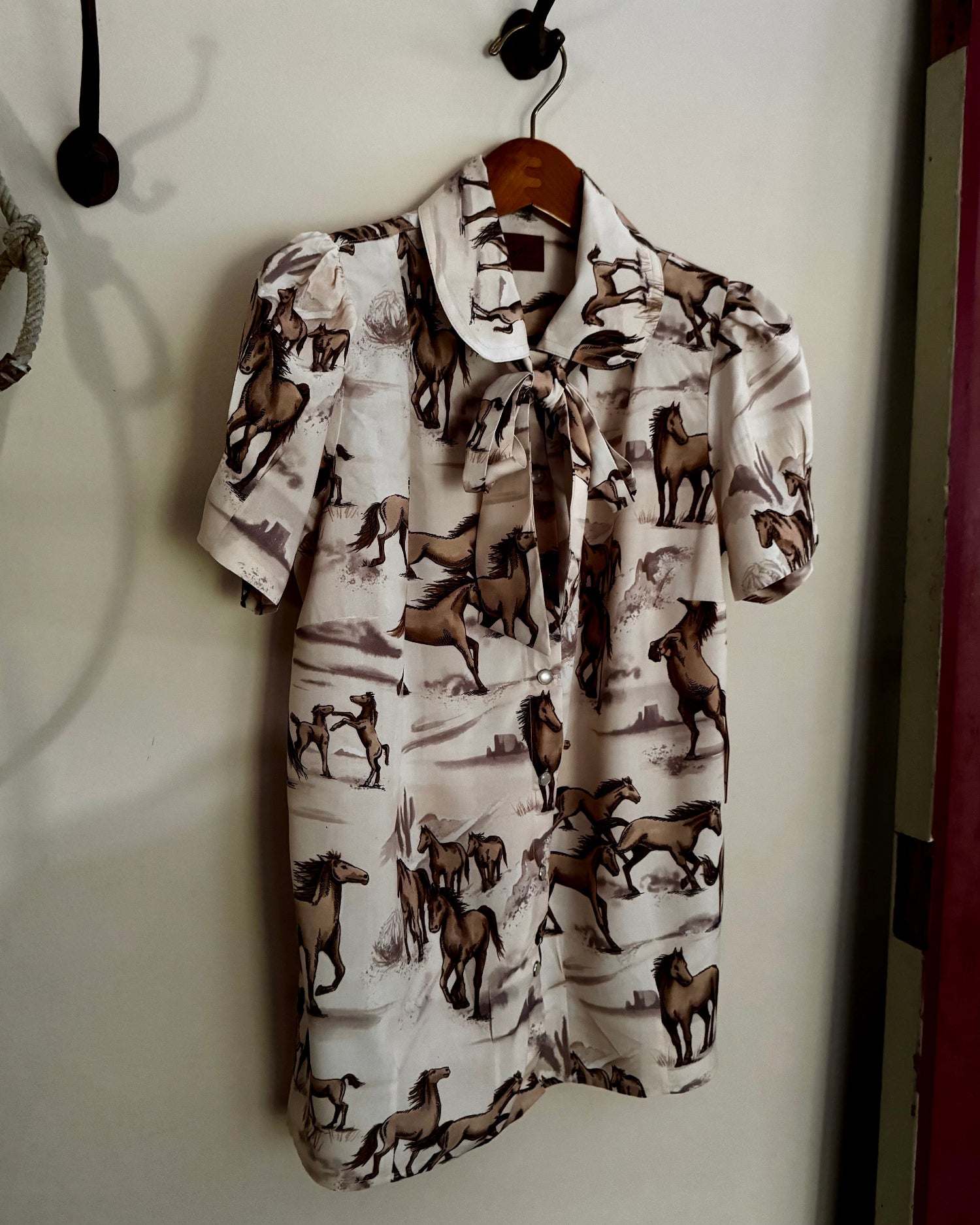 Shirt with horse pattern hanging on a hook against a white wall.