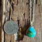 Turquoise pendant necklace on a wooden surface with a coin for scale