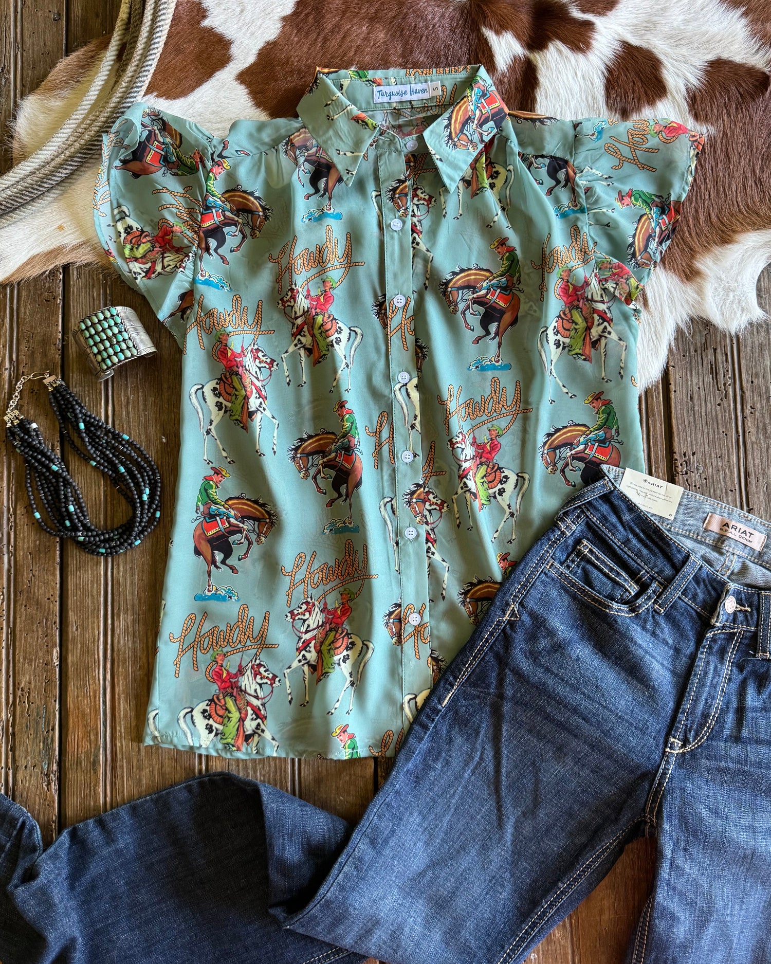 Retro cowboy patterned shirt and jeans on a wooden surface with cowhide rug