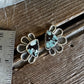 A pair of silver-toned stud earrings with triangular turquoise-blue and black marbled stone centers, displayed on a rustic wooden surface next to a metal ruler for scale.