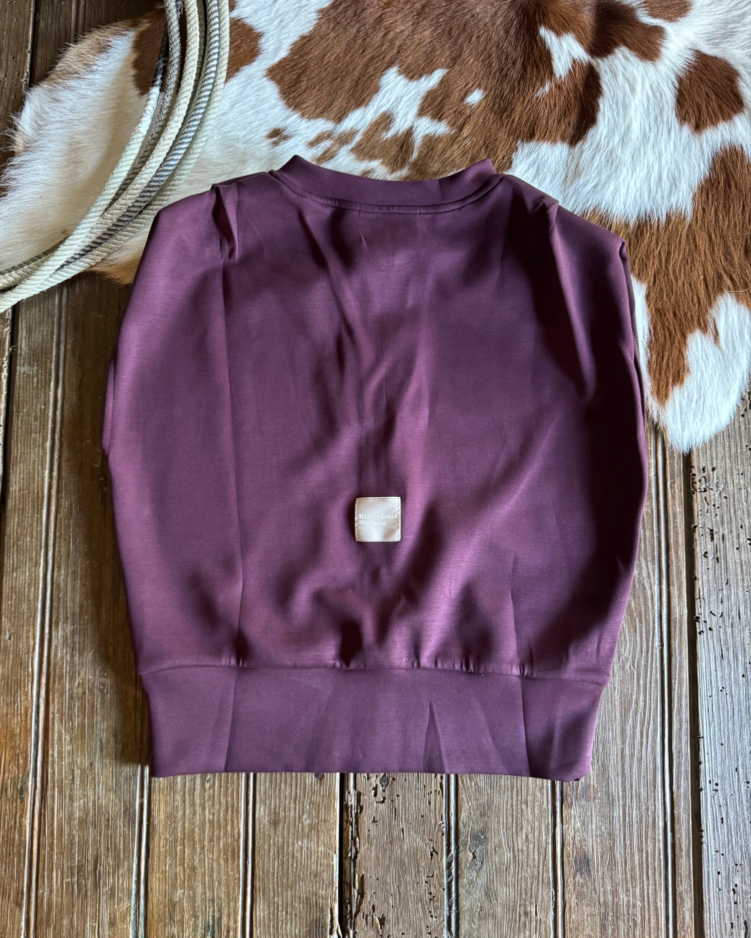 Purple sleeveless top on a wooden surface with a cowhide rug in the background
