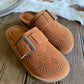 Pair of tan loafers with metallic buckles on a wooden surface.