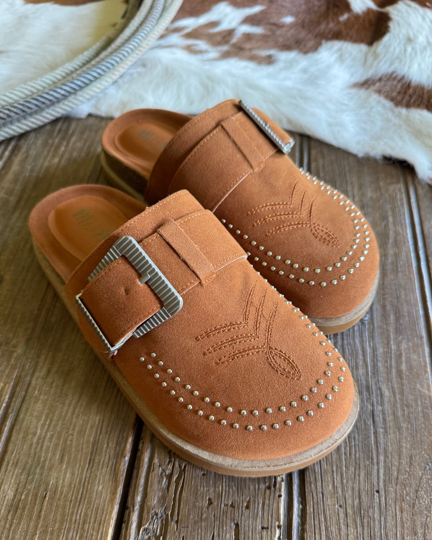 Pair of tan loafers with metallic buckles on a wooden surface.