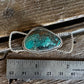 A silver-toned ring with a rough turquoise stone, shown on a rustic wooden surface next to a stainless steel ruler for scale.